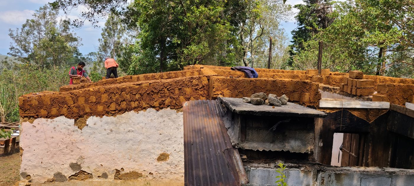 Two men laying new adobe bricks on top of the walls of the old house