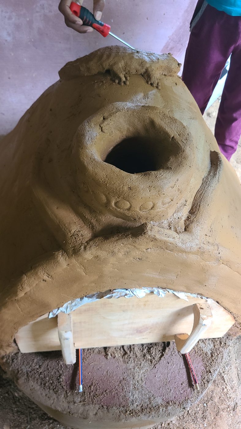 The cob oven being shaped by hand, with a clay lizard on top