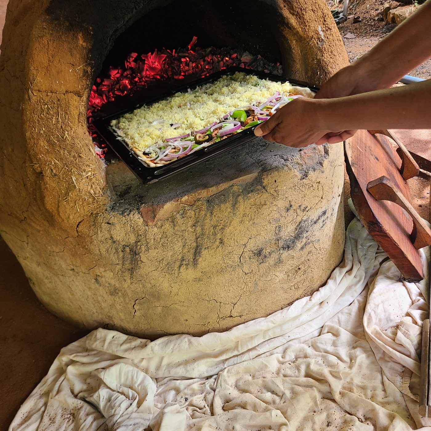 A tray of pizza going into the glowing cob oven