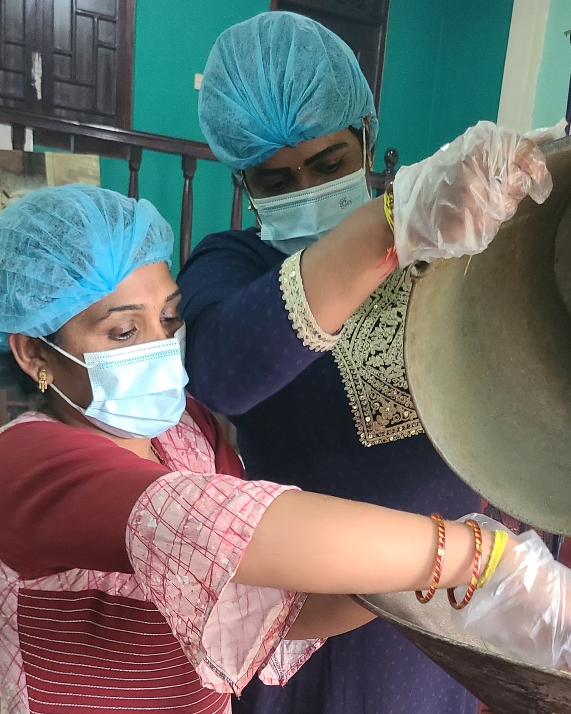 Pushpa and Kumari pouring cacao beans into the roasting machine