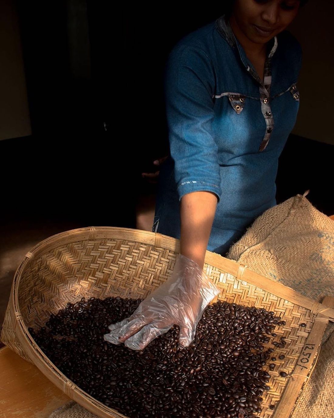 A member of the roastery team sorting roasted beans by hand in a woven basket